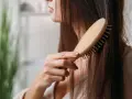 Eine Frau kämmt ihr langes, dunkles Haar mit einer Holzbürste. Sie achtet auf ihre Haare, um Haarausfall bei Frauen im Alter vorzubeugen.