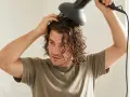 Ein junger Mann mit wellen haaren föhnt sich die Locken mit einem Diffusor.