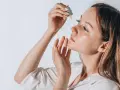Frauenhand trägt Tropfen eines Serums auf ihr Gesicht auf. Ob Squalan oder Hyaluron, die Haut strahlt Feuchtigkeit aus.
