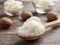 Ein Holzlöffel voller cremiger shea butter haare, daneben Nüsse und Schalen mit der Butter.