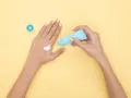 Hände mit Creme, die Glycerin enthält, auf gelbem Hintergrund.