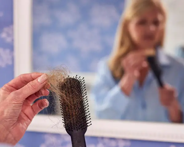 Frauen mit Haarausfall halten eine Bürste mit vielen Haaren. Im Spiegel sieht man eine Frau, die sich die Haare kämmt.