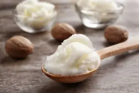 Ein Holzlöffel voller cremiger shea butter haare, daneben Nüsse und Schalen mit der Butter.