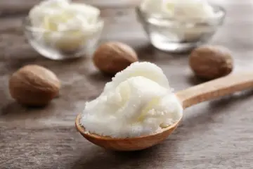 Ein Holzlöffel voller cremiger shea butter haare, daneben Nüsse und Schalen mit der Butter.