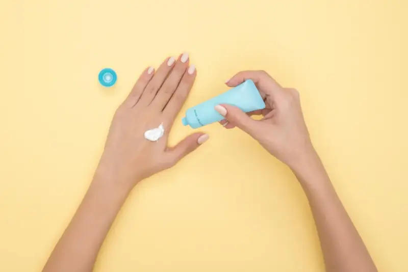 Hände mit Creme, die Glycerin enthält, auf gelbem Hintergrund.